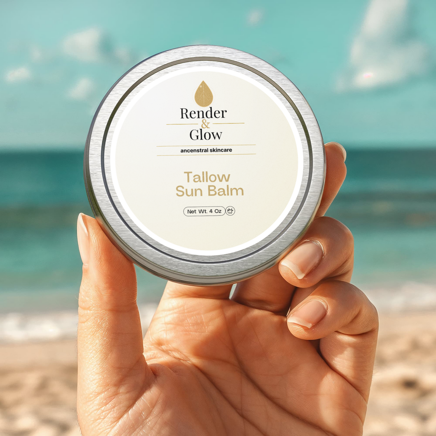 Hand holding a tin of Render & Glow Tallow Sun Balm, with a beach and ocean blurred in the background.
