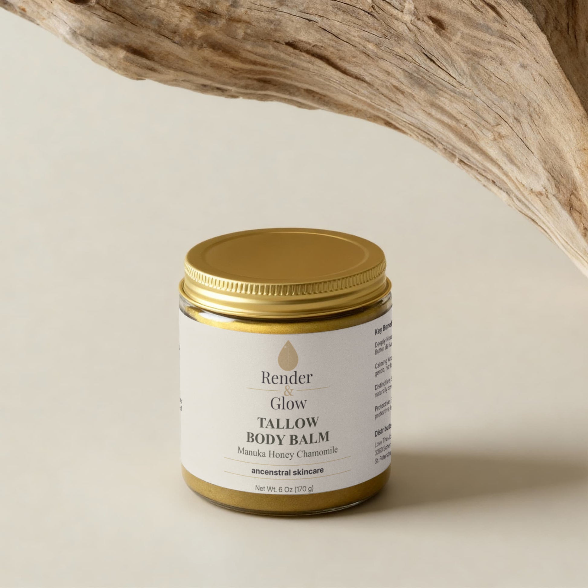 A jar of Render & Glow Tallow Body Balm rests on a beige surface below a textured wooden branch.