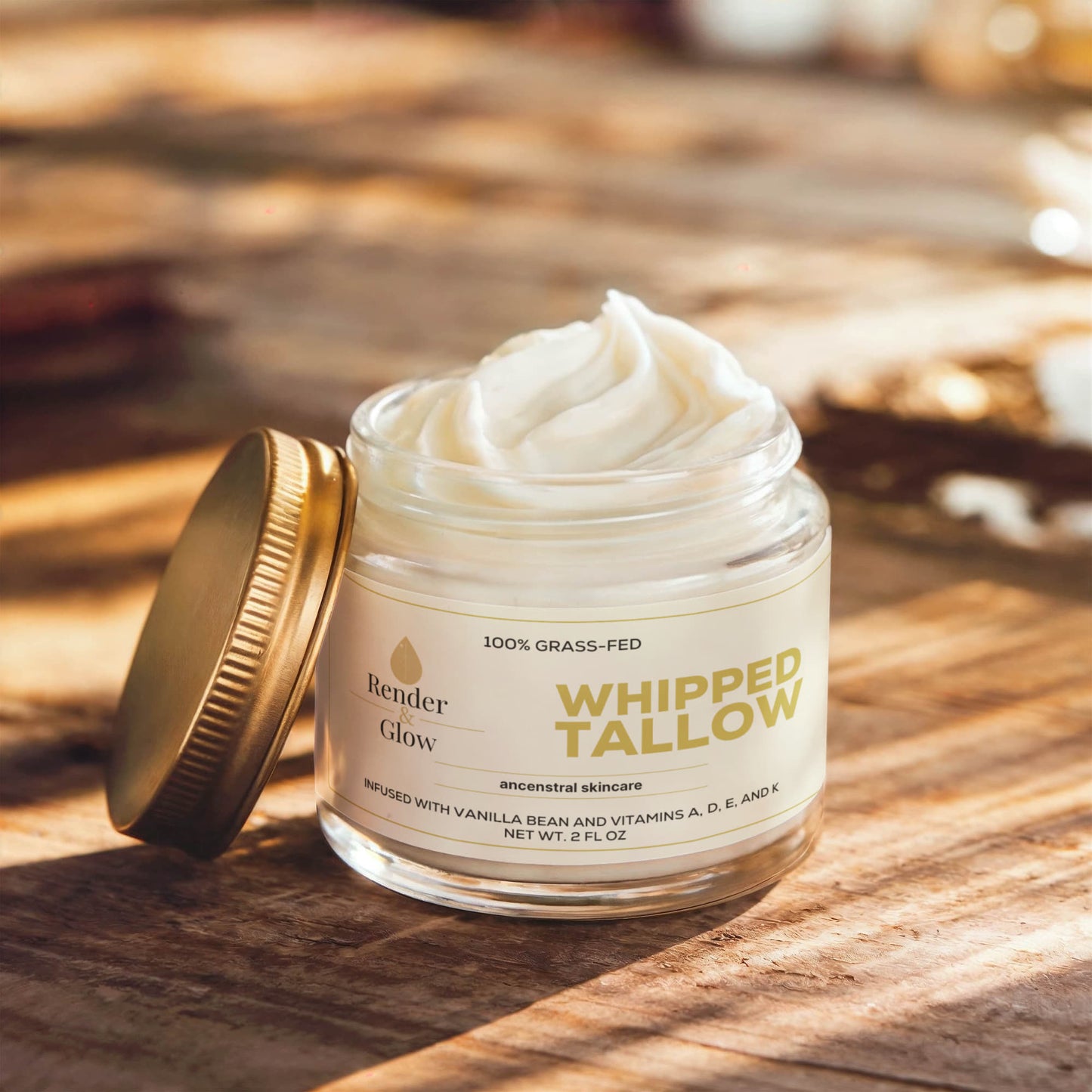 A jar of Render & Glow Whipped Tallow Skin Balm with a gold lid glows in sunlight on wood.