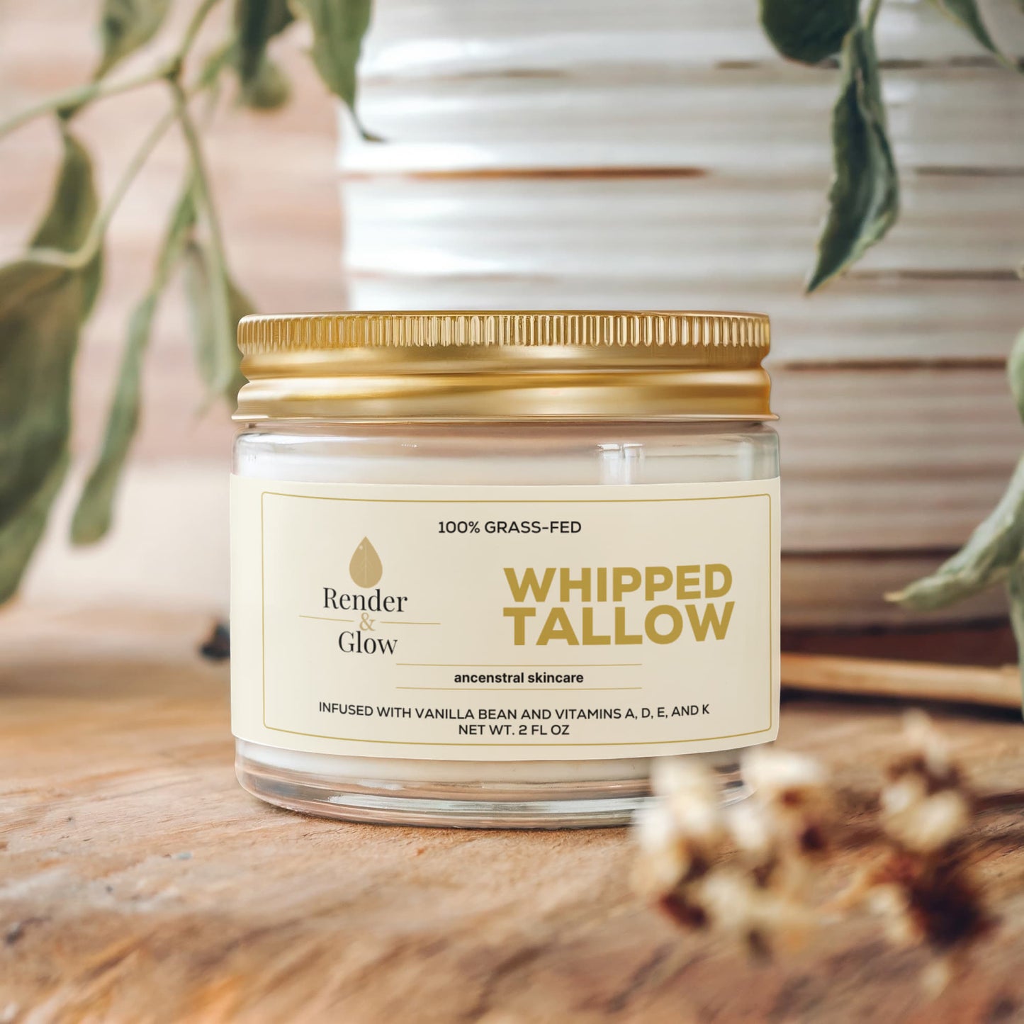 A jar of Render & Glow Whipped Tallow Skin Balm with a gold lid rests on wood, surrounded by plants.
