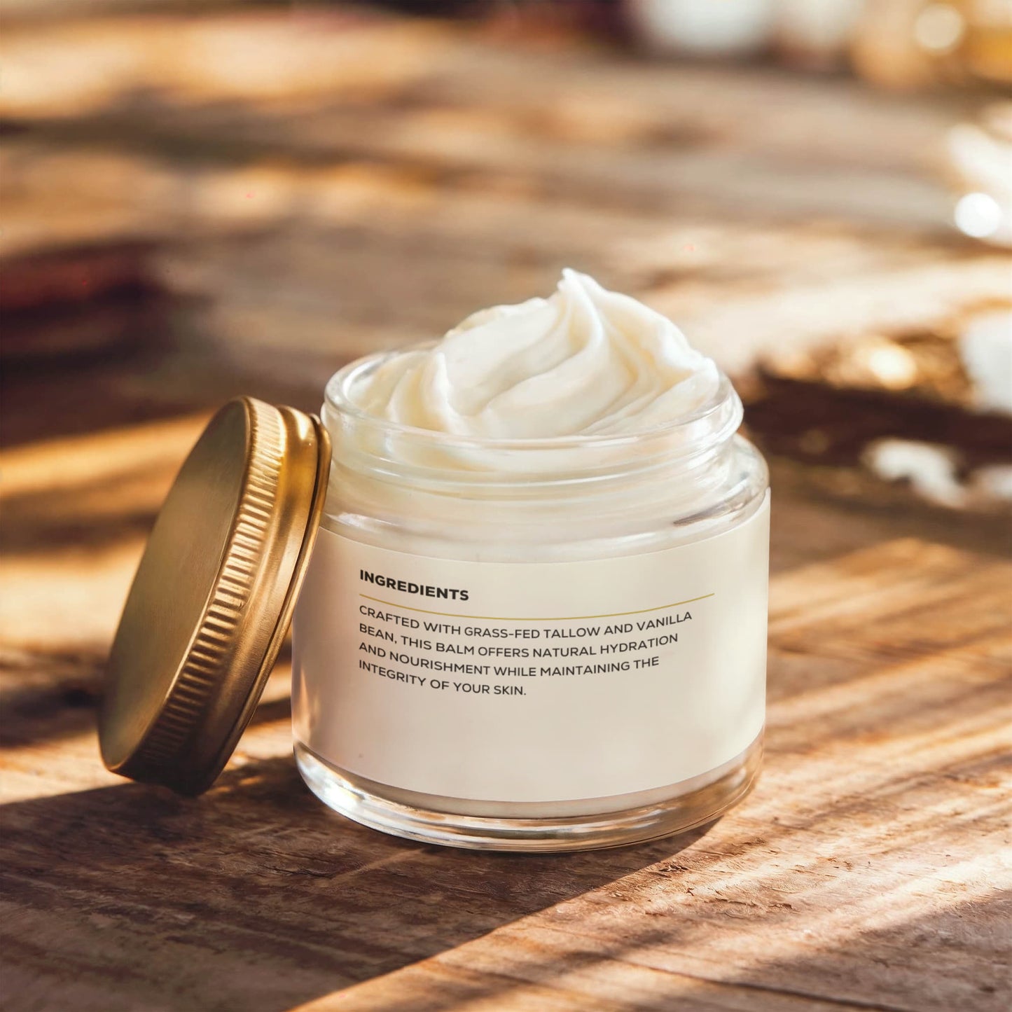 A glass jar of Render & Glow Whipped Tallow Skin Balm with a gold lid sits open on a wooden surface in warm light.