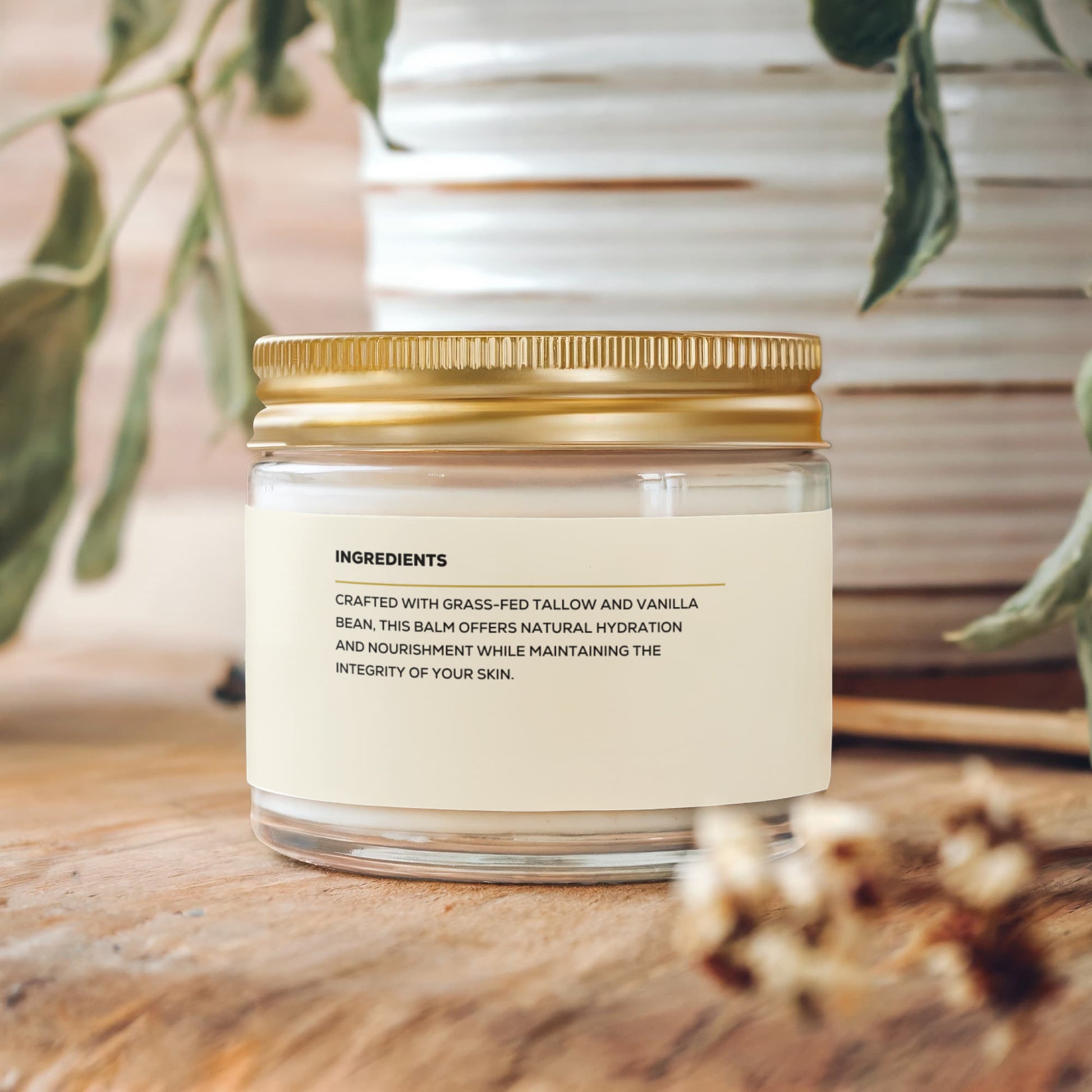 A glass jar of Render & Glow Whipped Tallow Skin Balm with a gold lid rests on wood, plants in the background.